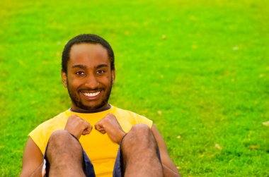 Yeşil çimenler ve ağaçlarla çevrili parkta oturuş lar yapan sarı gömlekgiyen adam, mutlu yüz ifadesi, eğitim konsepti