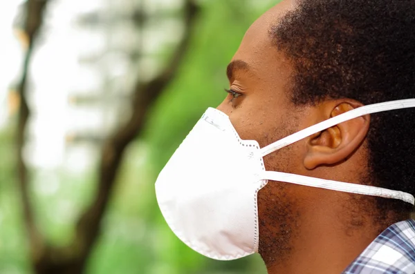 Penutup pria headshot profil sudut, meliputi hidung dan mulut dengan perlindungan filter topeng berjalan di luar, biru pohon latar belakang — Stok Foto