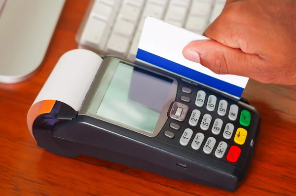 Крупный план ручной кражи кредитной карты через платежный терминал устройства, сидя на деревянной поверхности — стоковое фото