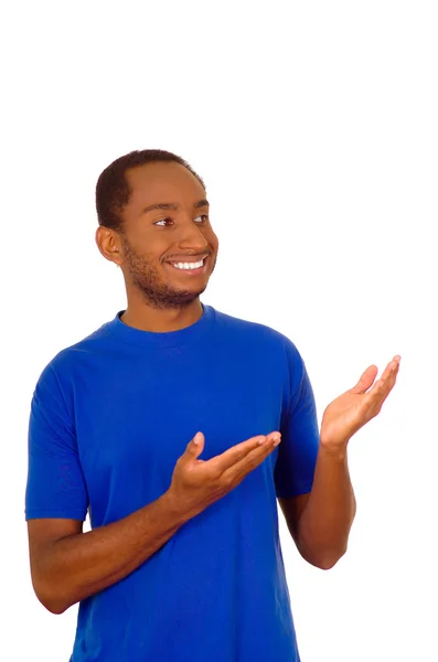 Homem vestindo forte camiseta azul de pé e interagindo usando mãos simulando apresentação enquanto sorri, fundo estúdio branco — Fotografia de Stock