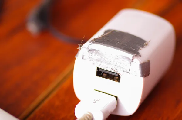 USB-kabel van de mobiele lader en blok liggen op houten ondergrond, zilveren Gaffatape tape gebruikt voor tijdelijke moeilijke situatie gebroken — Stockfoto