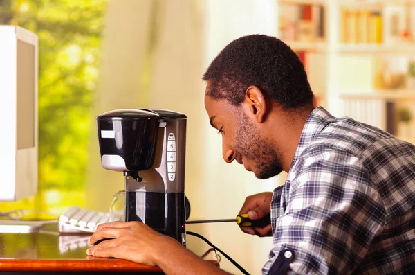 Man zittend door Bureau repareren kleine koffiezetapparaat met behulp van screwdiver, glimlachend gelukkig tijdens het werken — Stockfoto