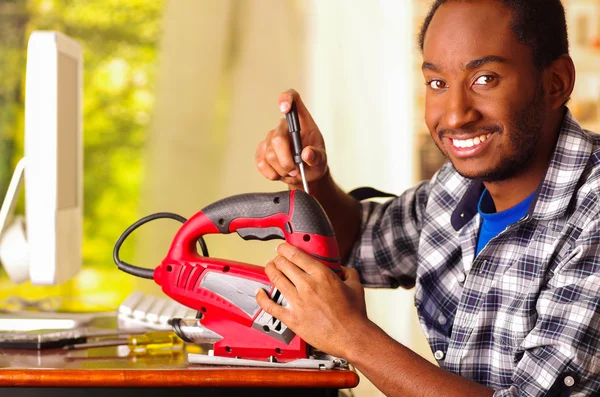 Hombre sentado junto al escritorio reparando rompecabezas de mano usando destornillador, sonriendo feliz mientras trabaja — Foto de Stock