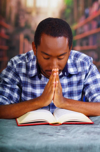 Uomo religioso seduto mentre prega e legge dal libro aperto sulla scrivania di fronte, concetto di religione — Foto Stock