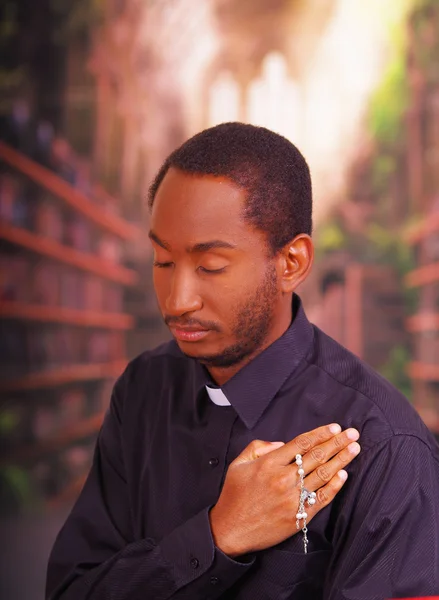 Sacerdote cattolico che indossa la tradizionale camicia del colletto clericale in piedi eseguendo segno della croce e tenendo in mano il rosario, concetto di religione — Foto Stock