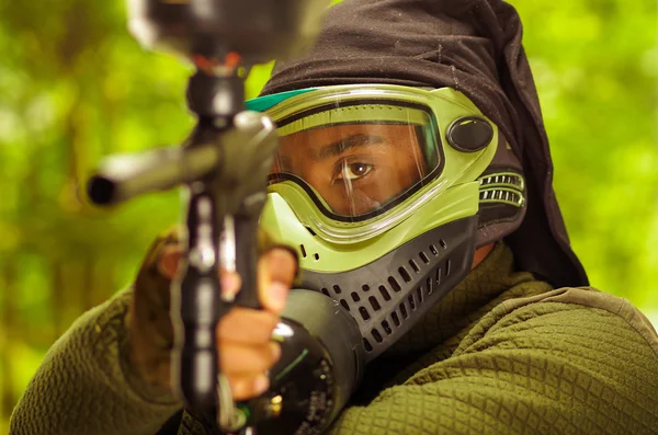 Closeup headshot homem vestindo verde e preto proteção máscara facial enfrentando câmera apontando paintball arma — Fotografia de Stock