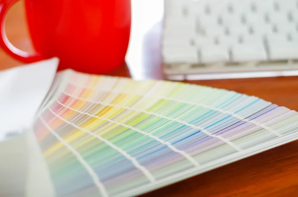 Closeup grande paleta colormap espalhado na frente do teclado do computador branco e caneca de café vermelho sentado na mesa de madeira, conceito de designer — Fotografia de Stock