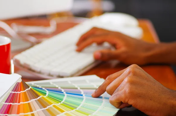 Main fermée tenant la palette, carte de couleurs étalée devant le clavier d'ordinateur blanc, concept de designer — Photo