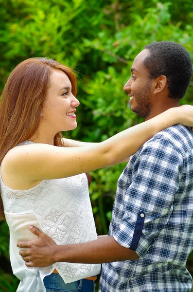 Casal encantador interracial vestindo roupas casuais abraçando e posando para câmera no ambiente ao ar livre — Fotografia de Stock