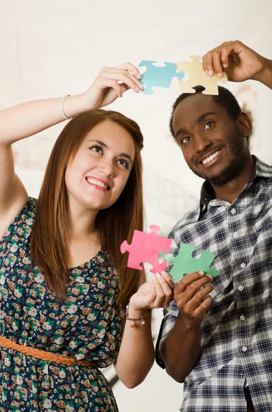 Interracial charming couple wearing casual clothes holding up large puzzle pieces and interacting happily, white studio background — Stock Photo, Image