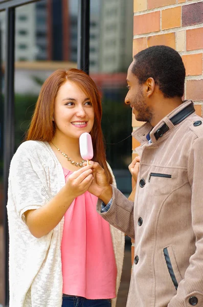 Interracial encantadora pareja usando ropa casual interactuando felizmente y compartiendo un helado — Foto de Stock