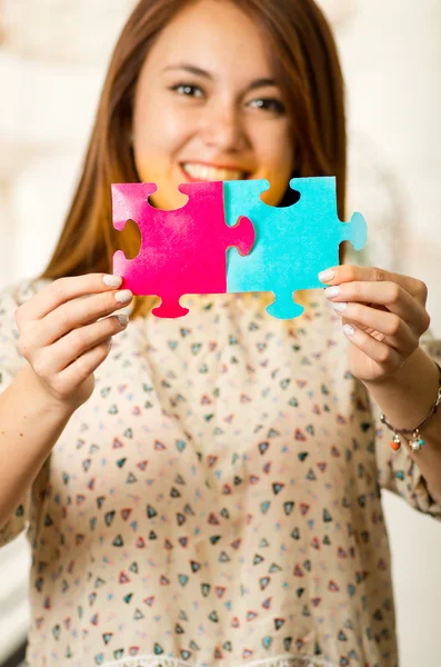 Šarmantní brunetka, která drží velké puzzle v růžové a modré a šťastně se usmívala na kameru, pozadí bílého studia — Stock fotografie