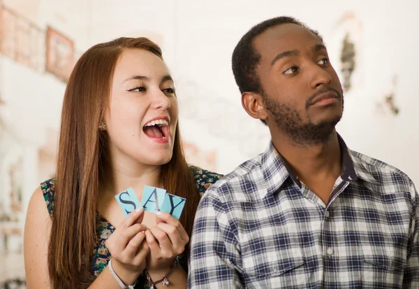 Charmig interracial par håller upp små bokstäver stava säga medan interagerar glatt, suddig Studio bakgrund — Stockfoto