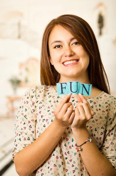 Cabeza encantadora morena mujer sosteniendo pequeñas letras deletreando la palabra diversión y sonriendo a la cámara — Foto de Stock