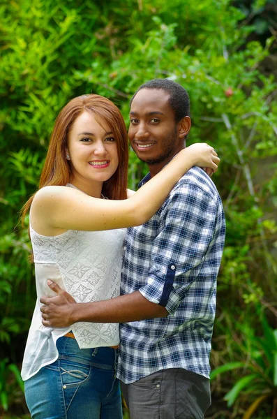 Interracial encantadora pareja con ropa casual abrazando y posando para la cámara en el ambiente al aire libre — Foto de Stock