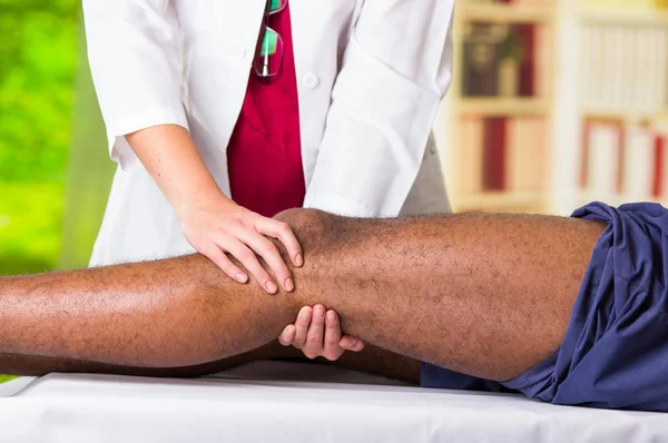 理学療法士から膝の治療を受ける男性、足を保持し、マッサージ、傷害医療概念を適用する彼女の手 — ストック写真