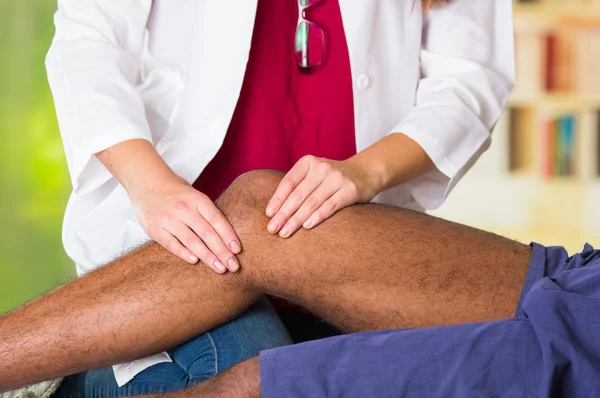 Hombre recibiendo tratamiento de rodilla de fisioterapeuta, sus manos sosteniendo su pierna y aplicando masaje, concepto médico lesión —  Fotos de Stock