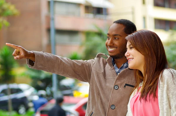 Interracial feliz encantadora pareja con ropa casual interactuando para la cámara en el entorno urbano al aire libre — Foto de Stock