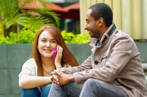 Interracial happy charming couple sitting on steps in front of building interacting and smiling for camera — Stock Photo, Image