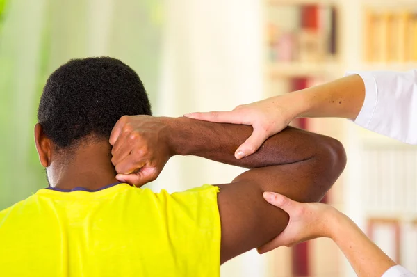 Hombre recibiendo tratamiento físico del brazo de fisioterapeuta, sus manos trabajando en su hombro y codo, concepto médico — Foto de Stock