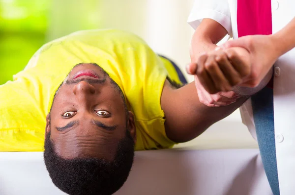 Man lying down getting physical shoulder treatment from physio therapist, patient looking into camera while her hands working on his upper arm area, medical concept — Stock Photo, Image