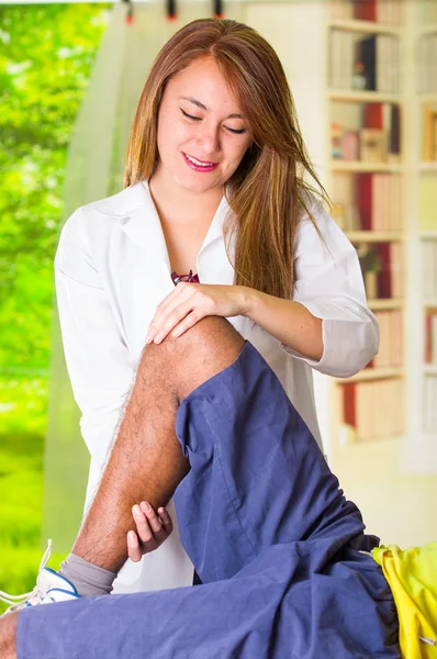 Мужчина получает лечение колена от физиотерапевта, ее руки держат его за ногу и применяют массаж, травма медицинской концепции — стоковое фото
