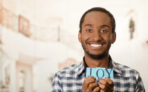 Headshot bel homme tenant de petites lettres orthographiant le mot joie et souriant à la caméra — Photo