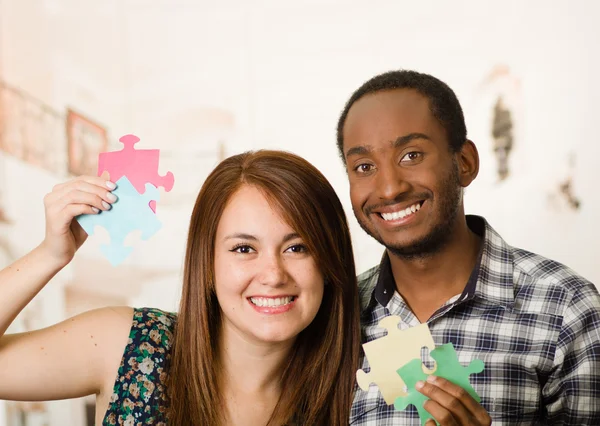 Interracial charming couple embracing friendly, holding up large puzzle pieces and happily interacting having fun, blurry studio background — Stock Photo, Image