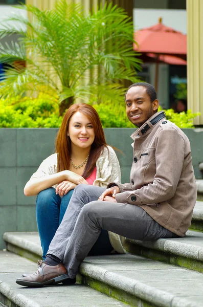 Interracial boldog bájos pár lépés előtt az épület egymásra, és mosolyogva kamera ül — Stock Fotó