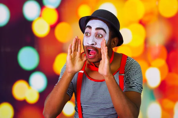 Headshot pantomime man met gezichts verf poseren voor de camera met behulp van handen rond mond schreeuwen, onscherpe achtergrond van de lichten — Stockfoto