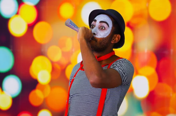 Cabeza pantomima hombre con pintura facial posando para la cámara usando cuerno de soplo, luces borrosas de fondo —  Fotos de Stock