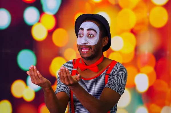 Homem pantomima com pintura facial posando para câmera segurando chifre de sopro, luzes embaçadas fundo — Fotografia de Stock