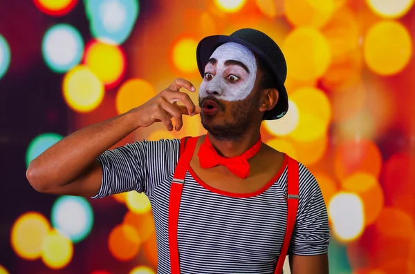 Pantomima hombre con pintura facial posando para la cámara, usando las manos interactuando lenguaje corporal, luces borrosas fondo —  Fotos de Stock