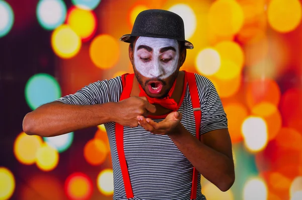 Homem pantomima vestindo pintura facial posando para câmera, usando as mãos interagindo linguagem corporal, luzes embaçadas fundo — Fotografia de Stock