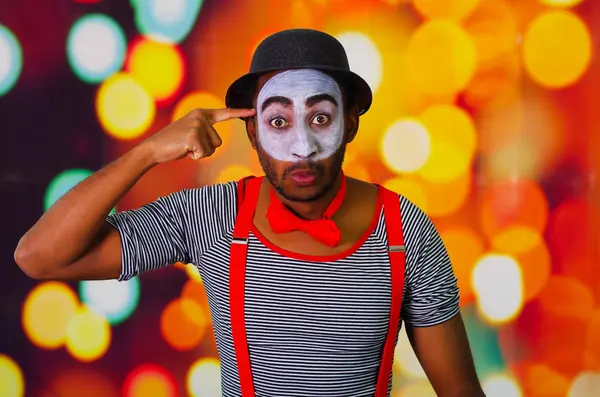 Pantomima hombre con pintura facial posando para la cámara, usando las manos interactuando lenguaje corporal, luces borrosas fondo — Foto de Stock