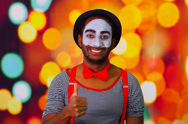 Pantomima hombre con pintura facial posando para la cámara interactuando dando pulgares hacia arriba sonriendo, luces borrosas fondo —  Fotos de Stock