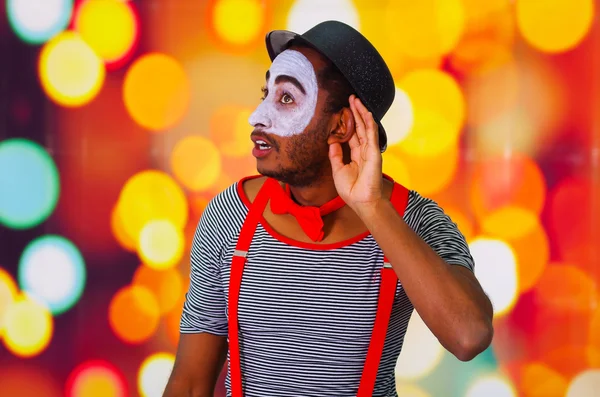 Человек-пантомима с лицевой краской позирует для камеры, используя руки взаимодействующие, размытые огни заднего плана — стоковое фото