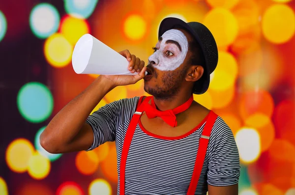 Pantomima uomo con pittura facciale in posa per la fotocamera che tiene il corno che soffia, luci sfocate sfondo — Foto Stock