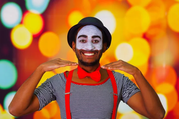 Pantomima hombre con pintura facial posando para cámara usando manos interactuando, luces borrosas fondo — Foto de Stock