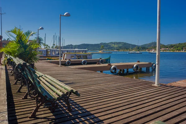 FLORIANOPOLIS, BRASIL - 08 DE MAYO DE 2016: algunos bancos en la parte superior del muelle cerca de algunos barcos estacionados y una bonita vista de algunas casas al final del lago — Foto de Stock