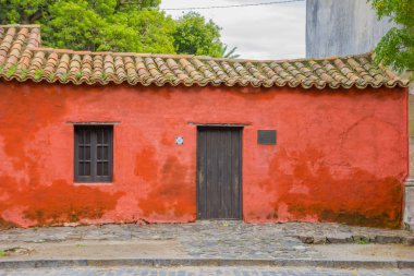 COLONIA DEL SACRAMENTO, URUGUAY - MAY 04, 2016: small little red house with a sign next to the door saying the year when the house was builded clipart