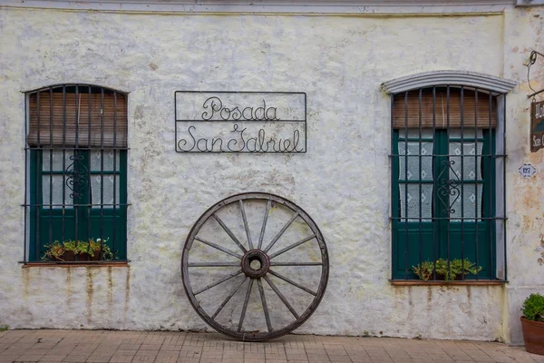 Colonia del sacramento, uruguay - 04. Mai 2016: Schild hängt an einer weißen alten Mauer mit zwei schönen alten grünen Fenstern und einem Wagenrad unter dem Schild — Stockfoto