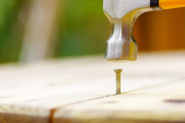 Hammer schlägt einen Nagel in ein Stück Holz — Stockfoto