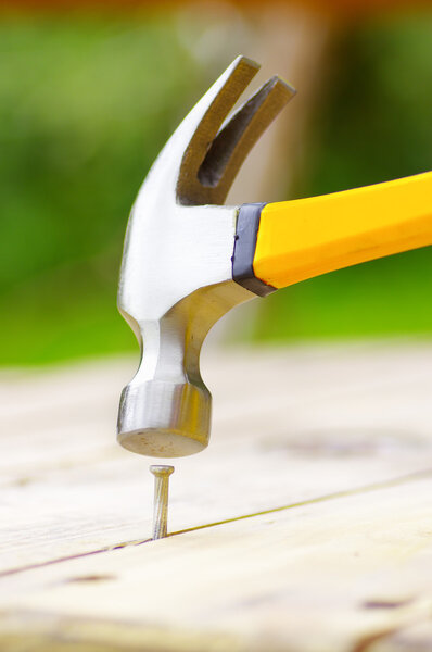 гвоздь стоит на куске дерева с молотком над ним
