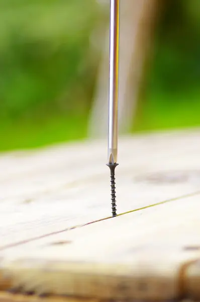 Zilveren schroevendraaier over een zwarte schroef op een tafel — Stockfoto