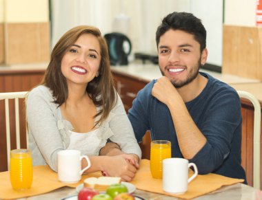 Genç çekici çift kamera, meyve, meyve suyu ve kahve gülümseyen kahvaltı masası tarafından oturmuş, önünde, hostel çevre yerleştirilir