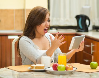 Kahvaltı Masası bakarak tablet ekran, meyve, meyve suyu ve kahve önde, yerleştirilen tarafından hostel çevre oturan genç güzel esmer