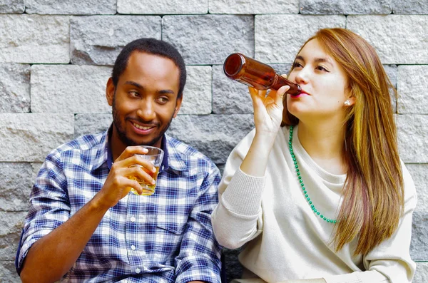 Couple Interracial portant des vêtements décontractés assis vers le mur de briques grises profitant de certaines boissons et de l'autre compagnie — Photo