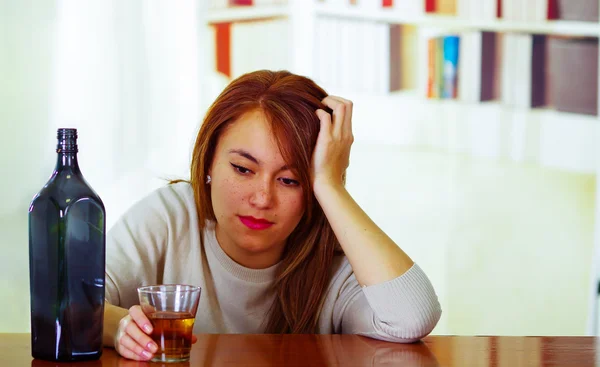 Attractive woman wearing white sweater sitting by bar counter lying over desk next to glass and bottle, drunk depressed facial expression, alcoholic concept — Stock Photo, Image