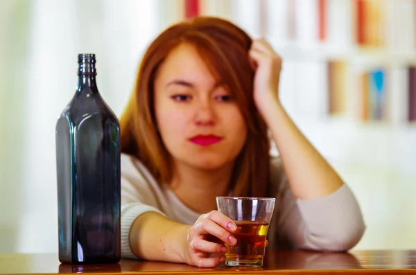 Attractive woman wearing white sweater sitting by bar counter lying over desk next to glass and bottle, drunk depressed facial expression, alcoholic concept — Stock Photo, Image